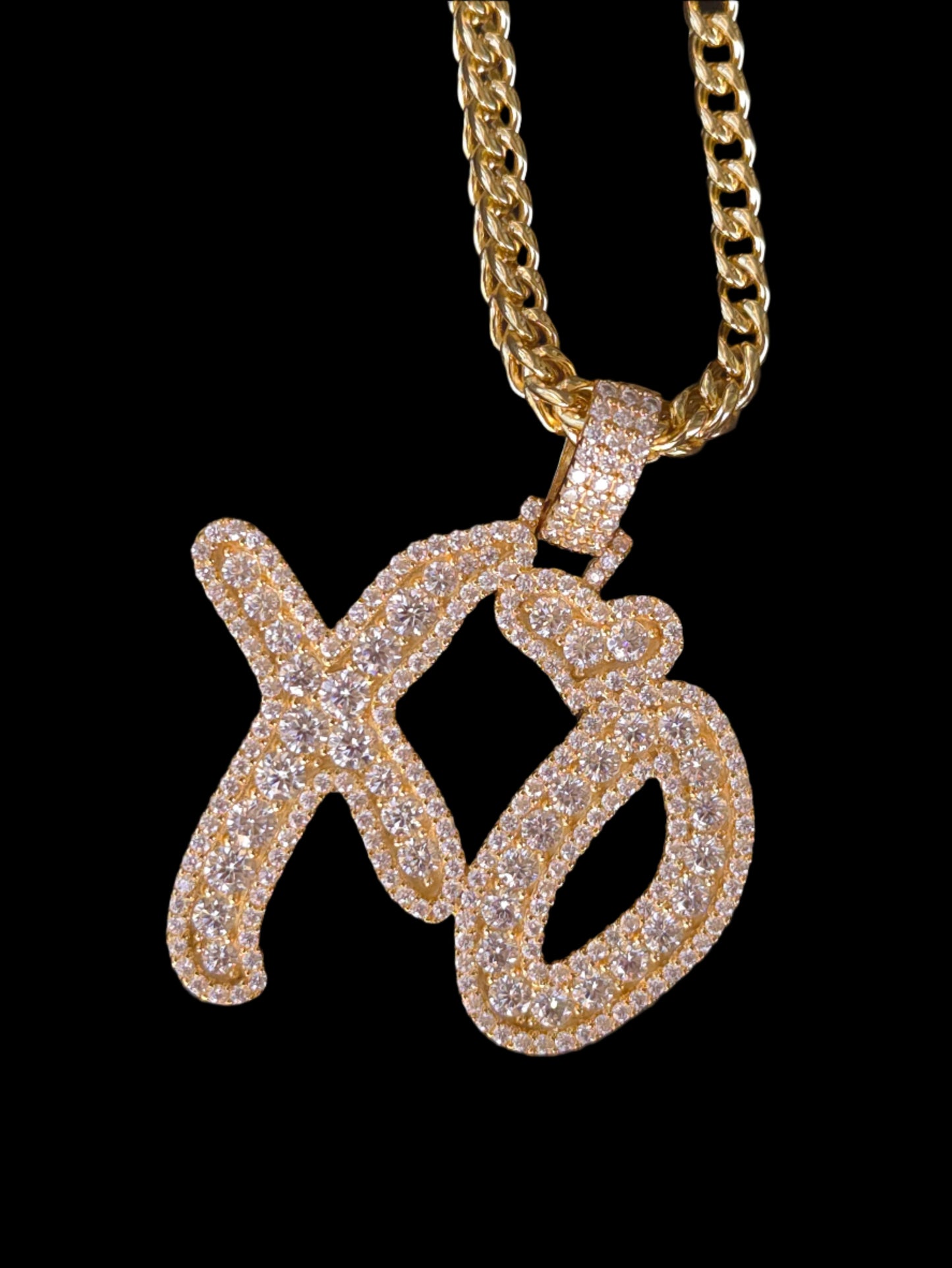 Gold chain with a diamond-encrusted letter 'Q' pendant on a dark textured background