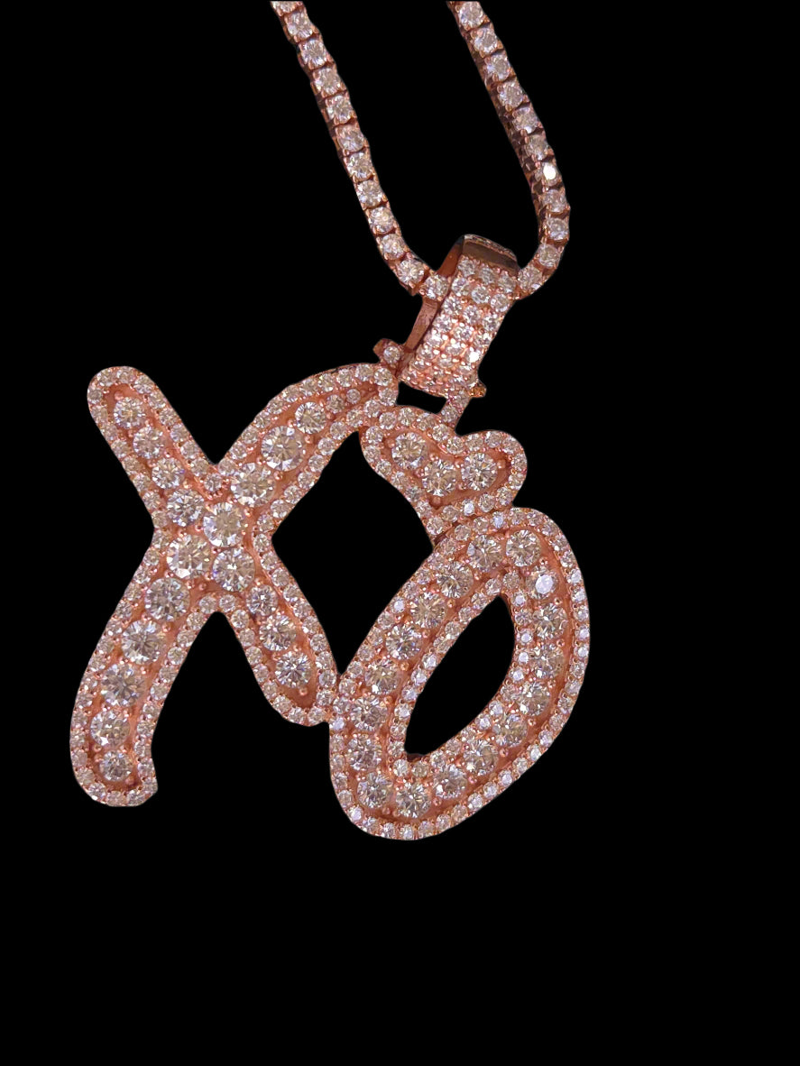 Rose gold necklace with a diamond-encrusted 'X' pendant on a dark textured background