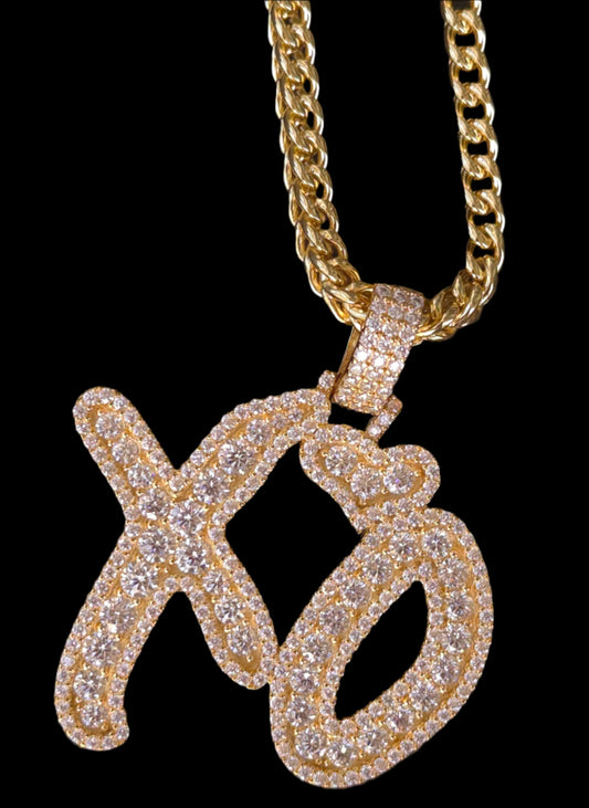 Gold chain with a diamond-encrusted letter 'Q' pendant on a dark textured background