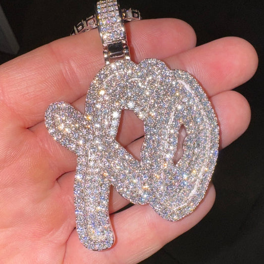 Silver xo pendant with the weeknd xo necklace design held in a hand against a dark background